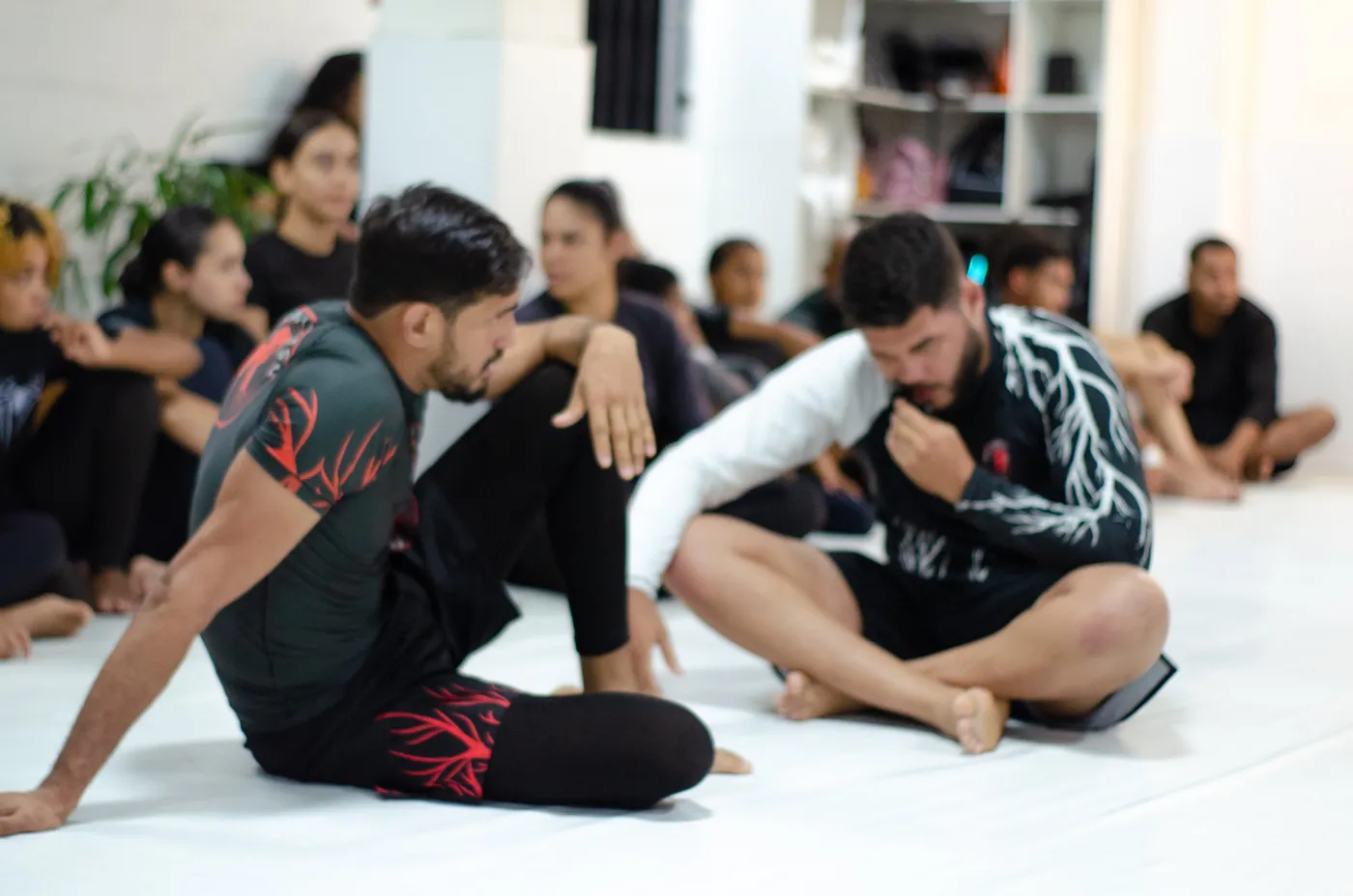 Alunos do CT Raiz Jiu-Jitsu 46 sentados no tatame durante a explicação da aula
